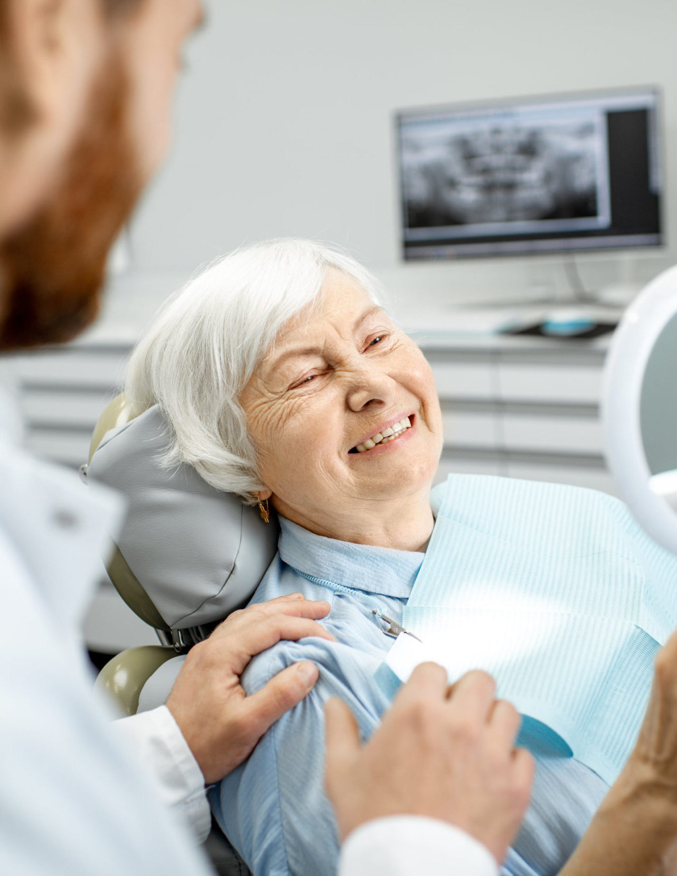 Happy elderly woman enjoying her beautiful toothy smile looking to the mirror in the dental office