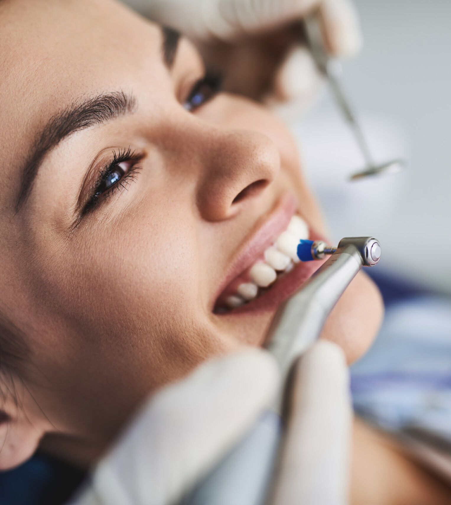 Close up portrait of pretty girl sitting in dental chair while stomatologist holding polisher and mirror. Girl is smiling