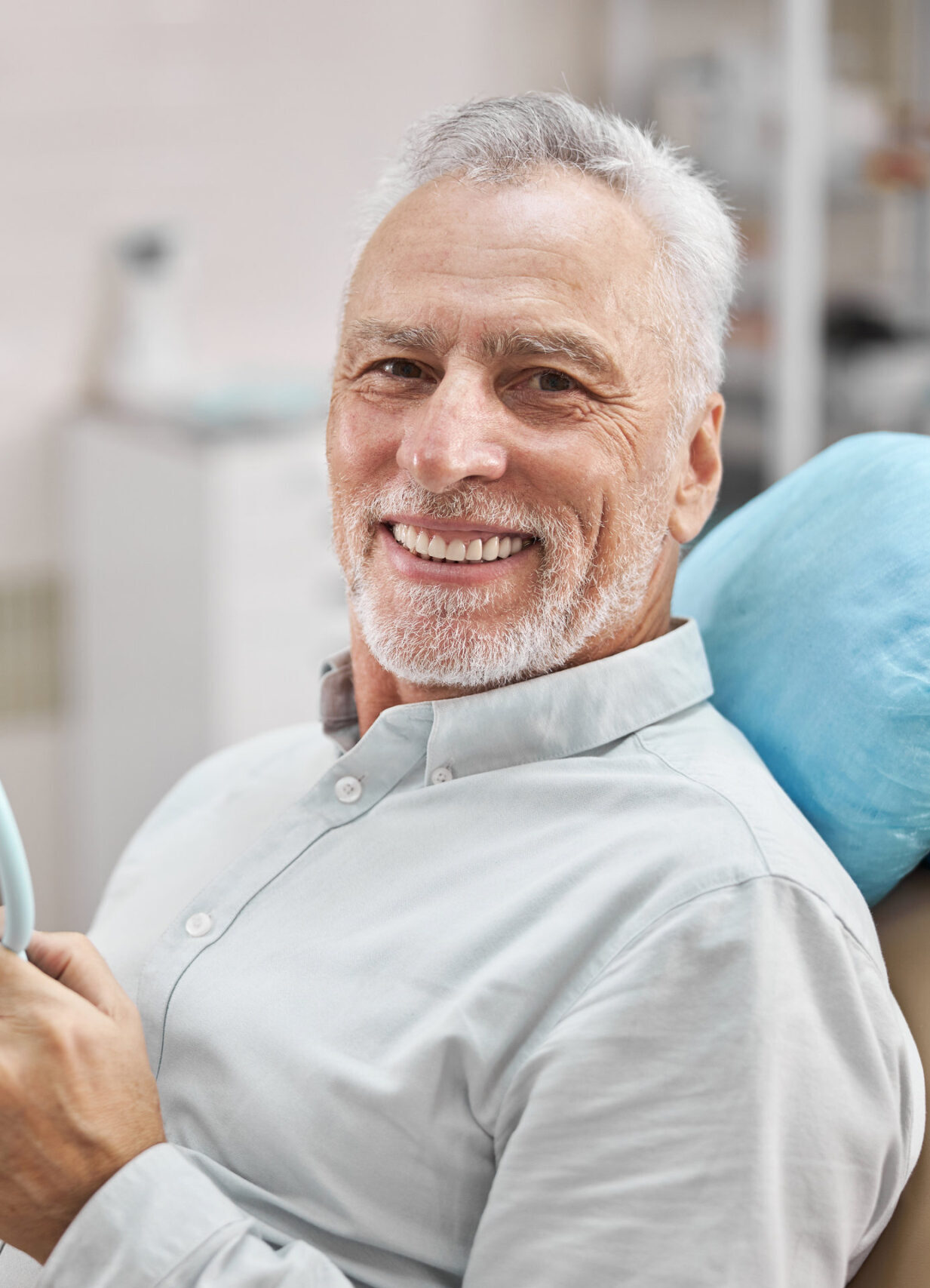 Cheerful patient sitting in a dental chair and holding a mirror while smiling at the camera
