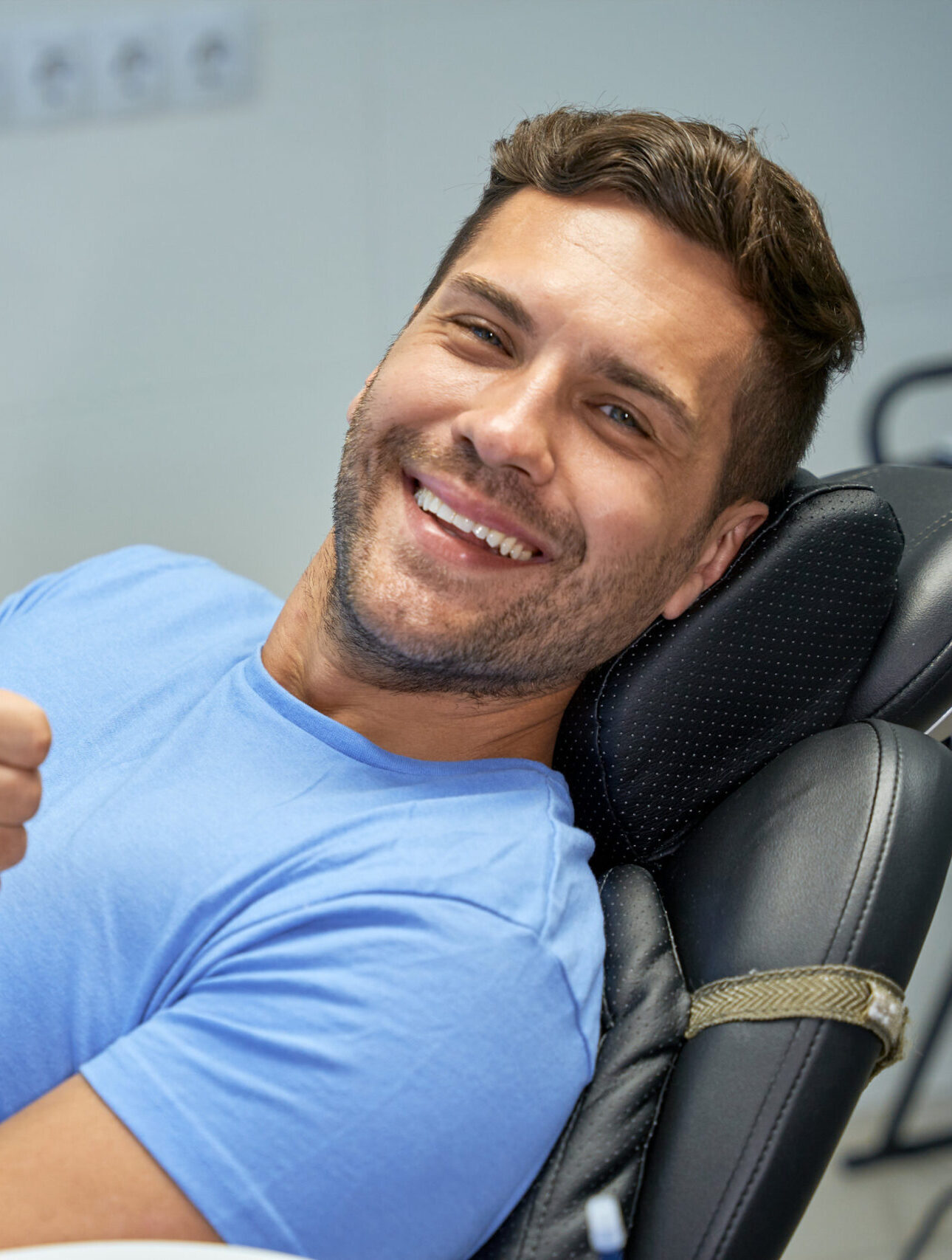Young brunette man smiling and showing thumbs up while leaning back in a dental chair