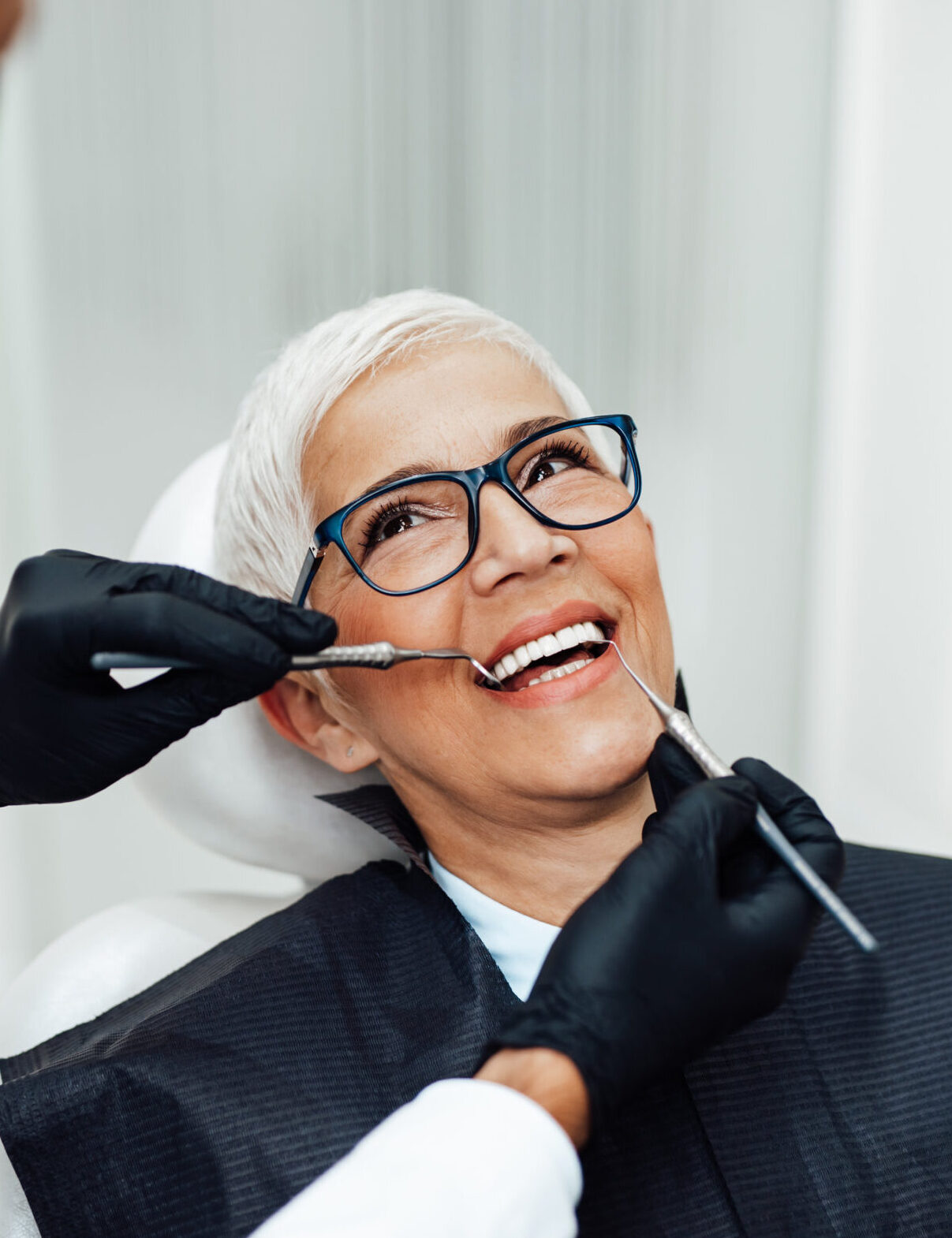 Beautiful senior woman having dental treatment at dentist's office. Dentist is wearing protective face mask due to coronavirus pandemic.
