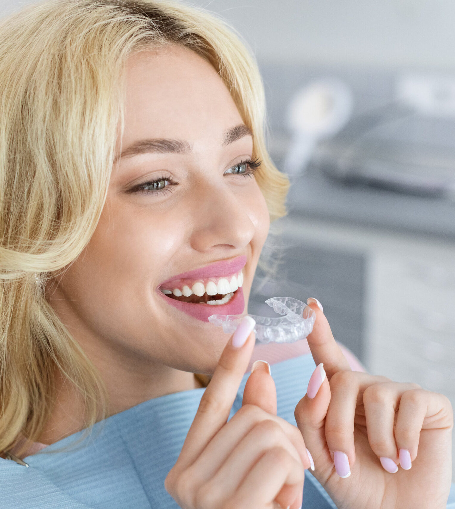 Invisalign orthodontics, modern dentistry concept. Happy young attractive blonde woman holding invisible braces or trainer while sitting at dental chair, closeup portrait, copy space