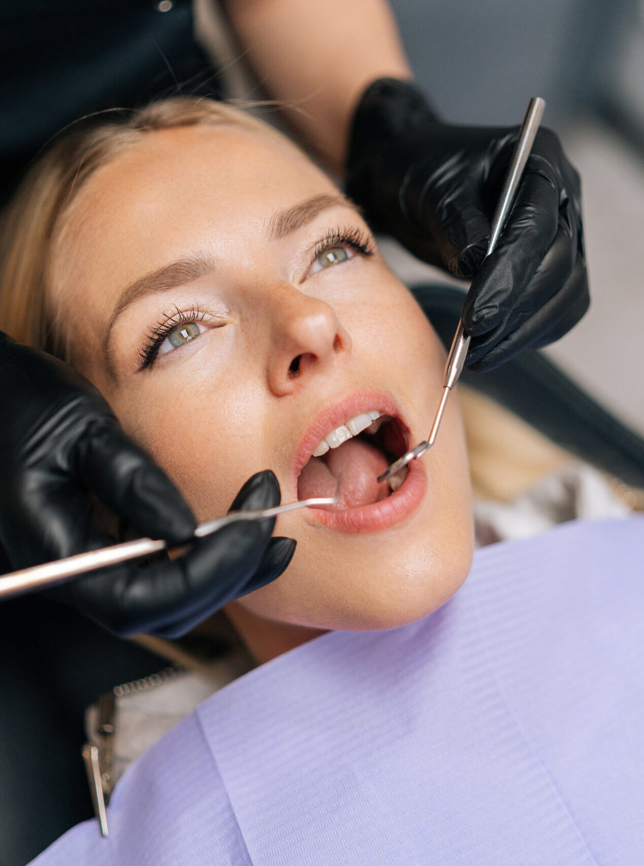 Closeup portrait of blonde female patient getting dental treatment in modern clinic, dentist doctor examining teeth of young woman with sterile tools in dentistry cabinet. Concept of dental health.